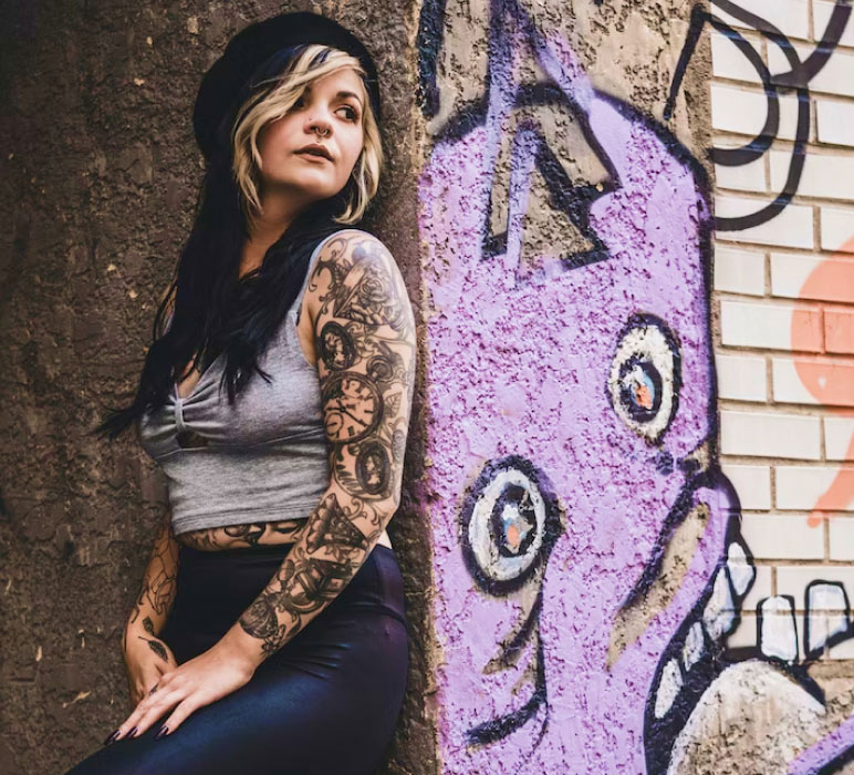 Woman with Tattooed Arms Standing Against Graffiti Wall